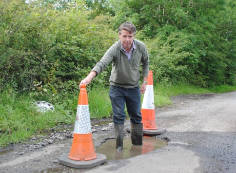 Councillor Anthony Feely stands in a deep pothole on the Tully Road, Garrison