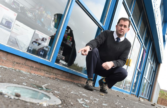 Ronan Reilly, understandably upset at the vandalism, points to broken glass and rocks at his shop front    RMG21